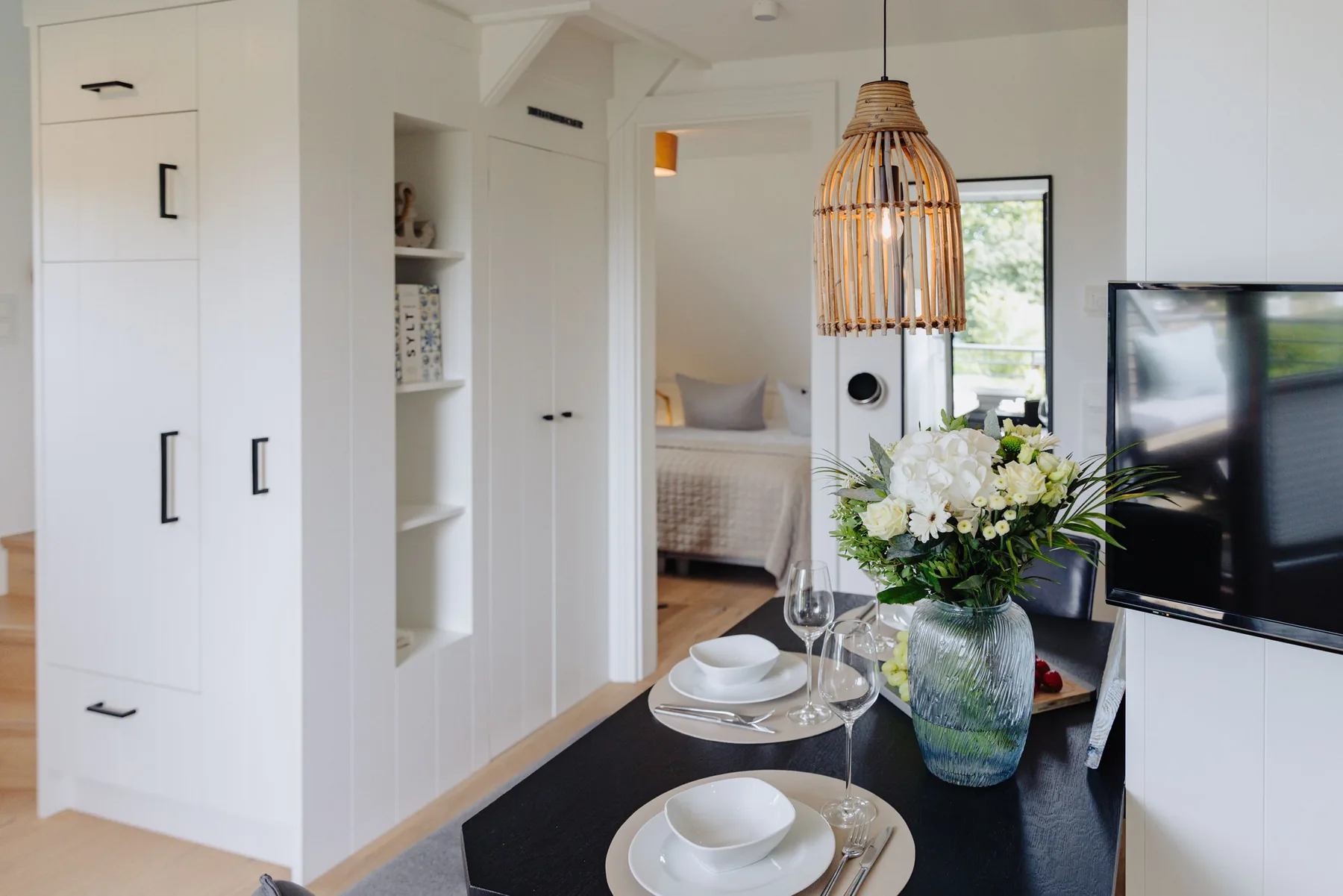 Ferienwohnung Wellenbrecher Sylt – Flur mit Rattanlampe und Blick ins Schlafzimmer
