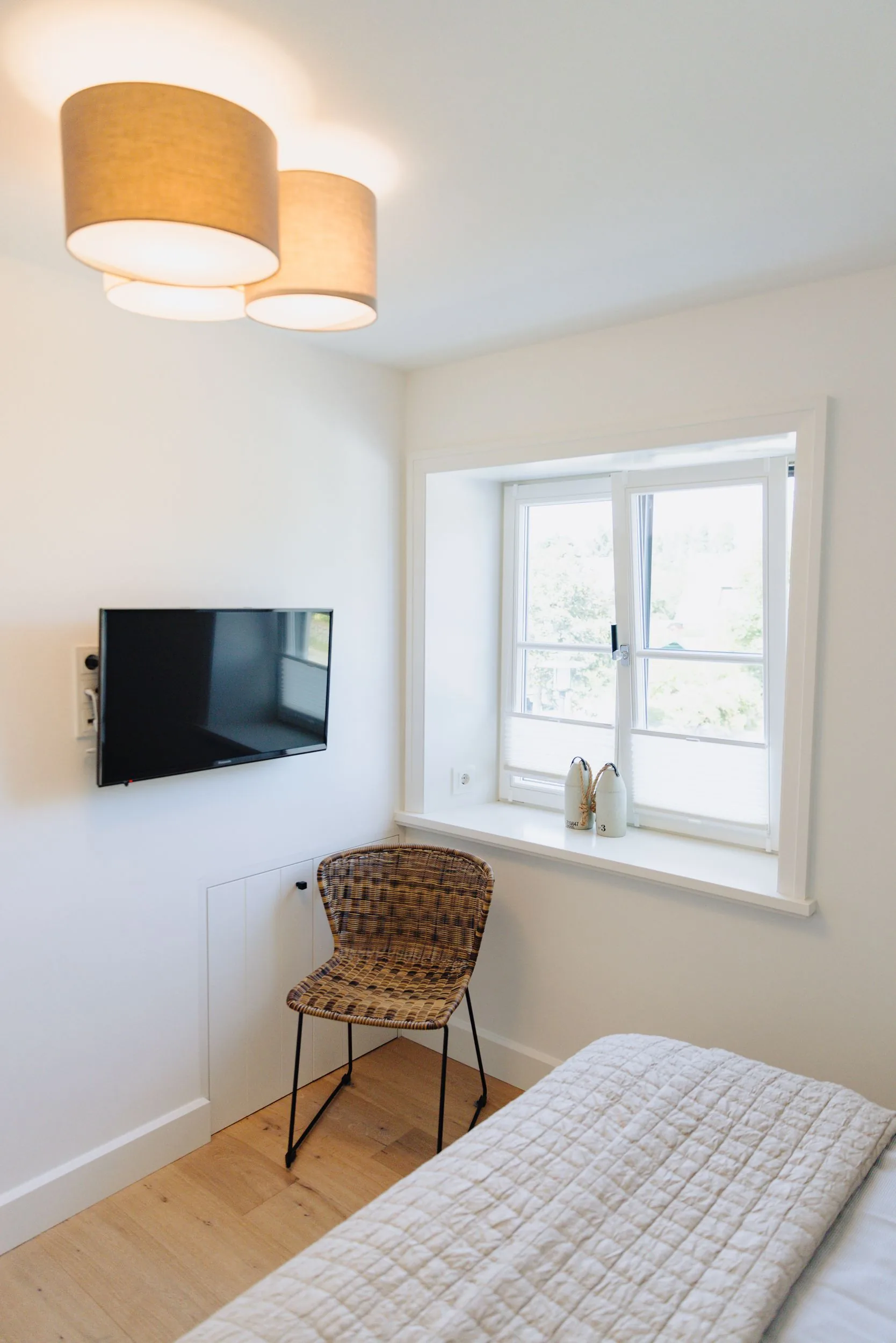 Ferienwohnung Wellenbrecher Sylt – Schlafzimmer mit Flatscreen-TV und Korbsessel